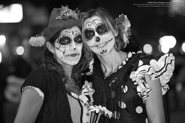 Black & white picture of two women with skeletal face paint and costume, celebrating  Dia De Los Muertos (Day of the Dead) in San Francisco, California.  