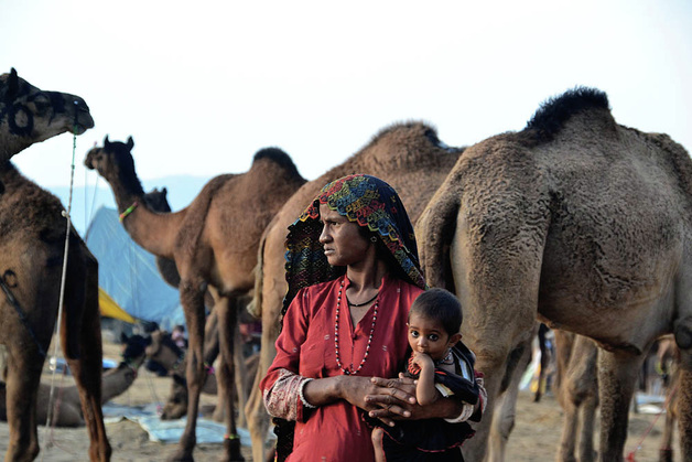 Picture of a woman holding her infant child in a refugee camp.  Camels and tents decorate the background.  Part of the Photographer Profiles series at FreePhotoCourse.com. © 2010, Soham Gupta, all rights reserved. 