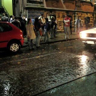 Picture of people on a city street corner at night while it is raining. Visit FreePhotoCourse.com for free photography lessons, tips, free pictures and more!