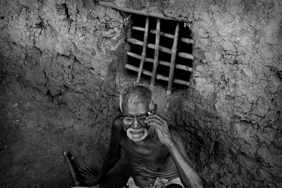Picture of an old man sitting in a primitive mud hut in India.  His window is a simple lattice of wooden sticks set into the mud.  Illustrates the desperate conditions for many of the country's inhabitants. Part of the Photographer Profiles series at FreePhotoCourse.com. © 2010, Soham Gupta, all rights reserved.      