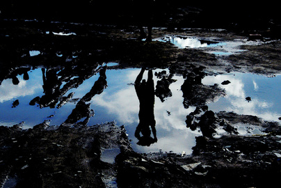 Beautiful artistic photography; picture depicts an abstract reflection of human figures and blue sky in puddles dotted in the soil. Part of the Photographer Profiles series at FreePhotoCourse.com. © 2010, Soham Gupta, all rights reserved.  